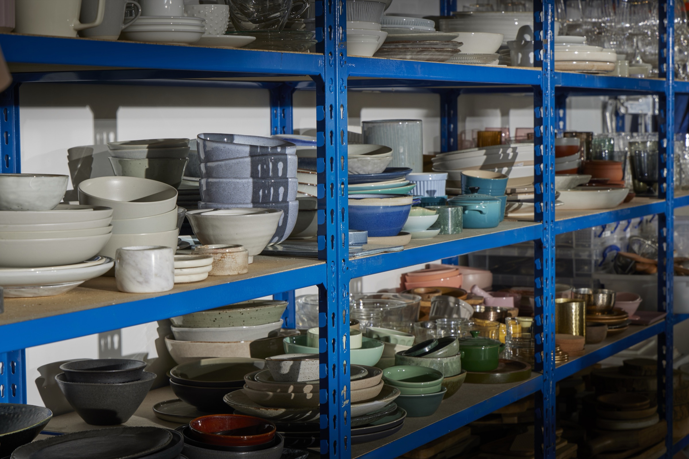 Open crockery shelves in the props store, grouped by colour